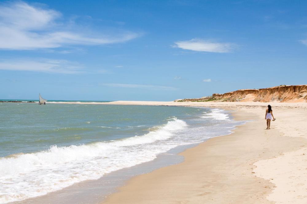 A woman strolls along the beach in Ceará, enjoying the serene coastal scenery and waves