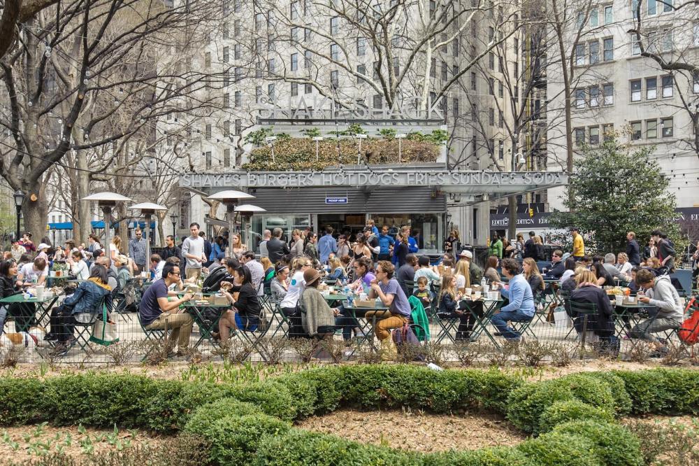 People are seated at tables outside at Shake Shack, enjoying food and conversation in a lively outdoor setting