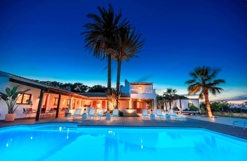 A large pool illuminated at night at the Es Pas Formentera Agroturismo villa, surrounded by serene landscaping