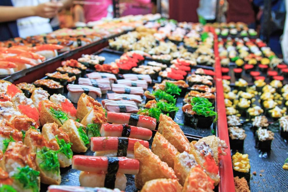 A large display of sushi arranged on a table at Tamsui Old Street Night Market, showcasing various types and colours