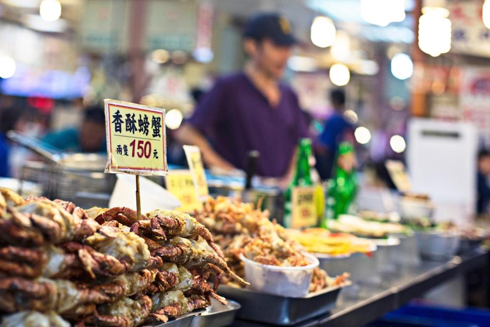 A man stands behind a counter at Keelung Miaokou Night Market, showcasing a variety of crabs and other food items.