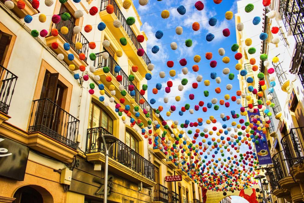 A vibrant street adorned with colourful paper lanterns, celebrating a festival in Spain