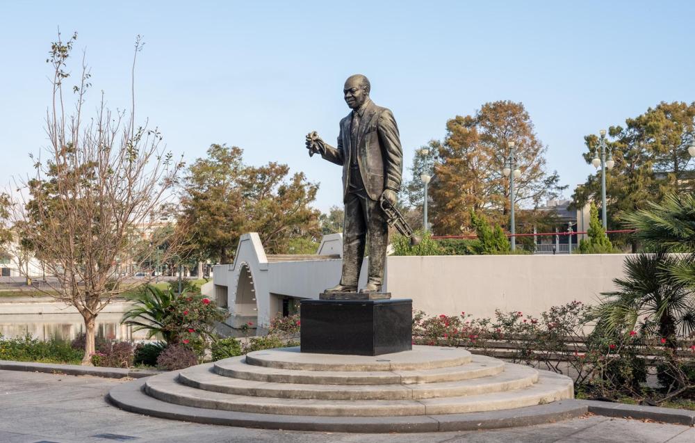 A statue of a Louis Armstrong stands prominently in Armstrong Park, surrounded by greenery and pathways