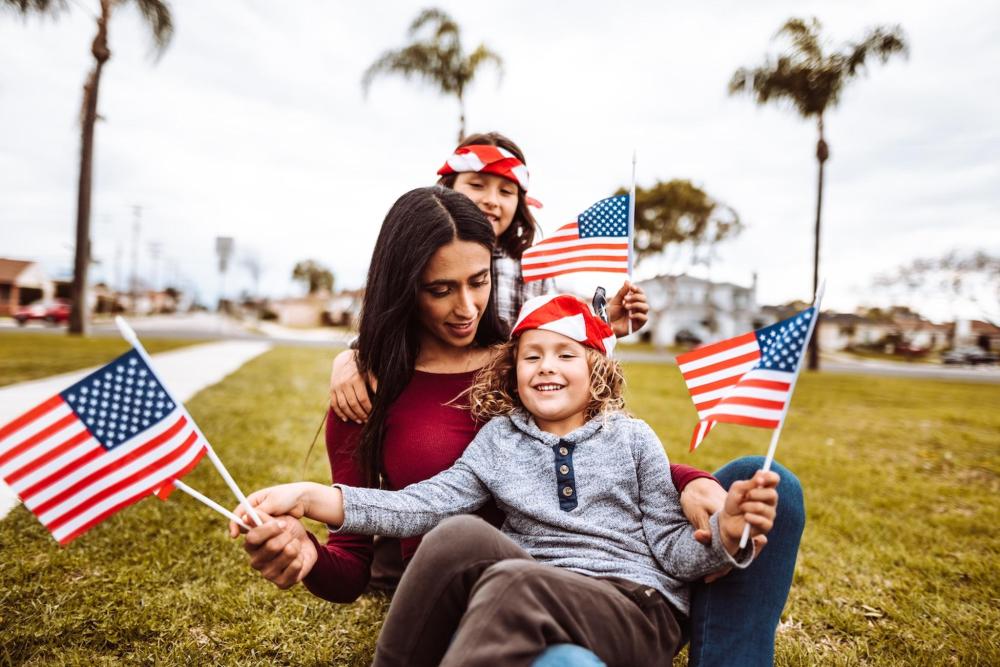 A woman and two children proudly hold the flag of the USA in a public park during a 4th of July celebration in NOLA