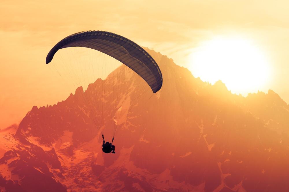 Paraglider soaring over Chamonix Valley mountains during a vibrant sunset, casting warm hues across the sky