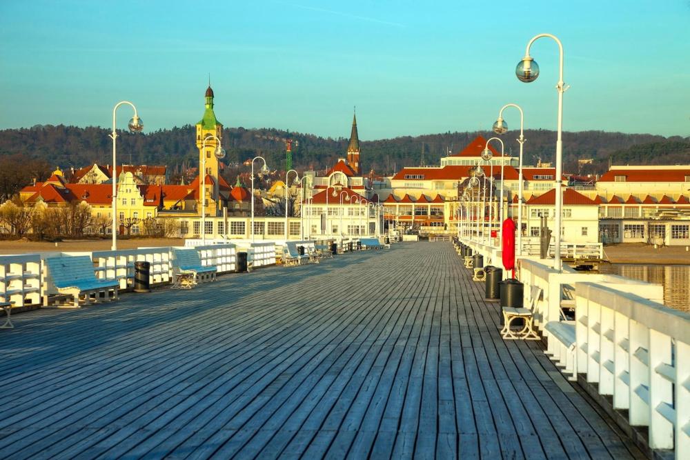 A wooden bridge with benches spans a scenic area, with a building visible in the background of Sopot