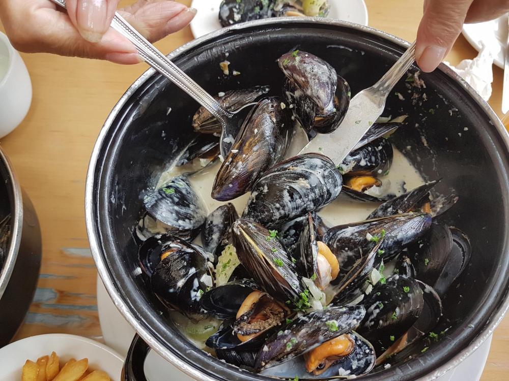 A person holding a spoon above a pot of mussels, preparing Moules à la crème