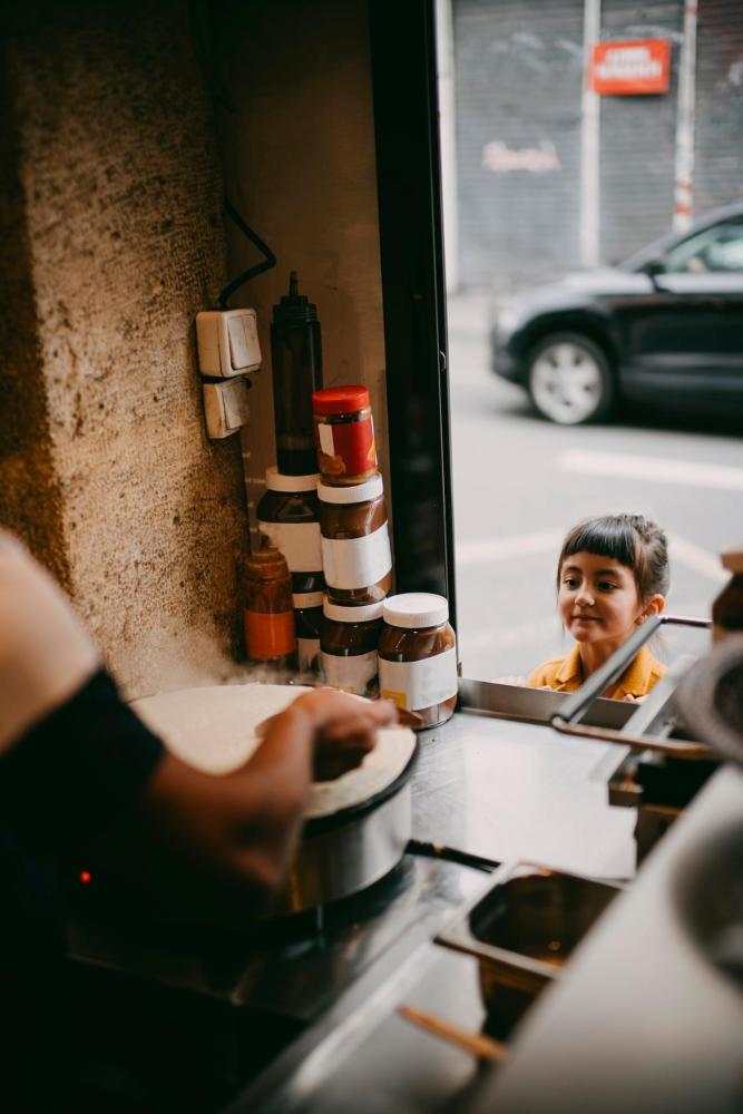 Some hands prepare a crêpe whilst a child waits in anticipation