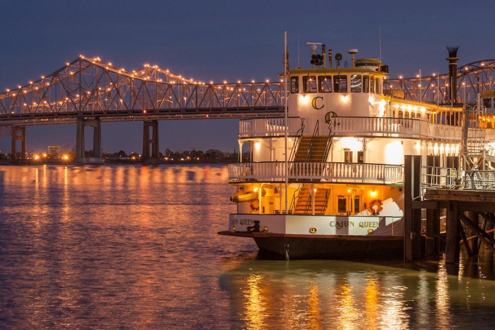 A large bridge spans the background, with the Riverboat New Orleans in the foreground, showcasing the city's scenic waterfront.