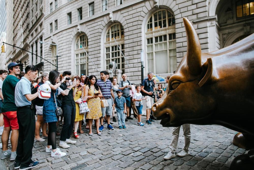 A group of people gathered around the iconic bull statue on Wall Street – a statue that symbolises financial strength and prosperity