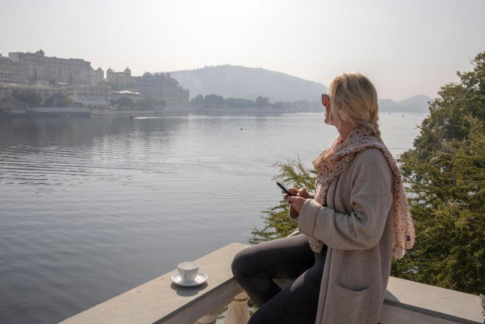 A woman drinks tea while sitting on a balcony overlooking Lake Pichola, Udaipur