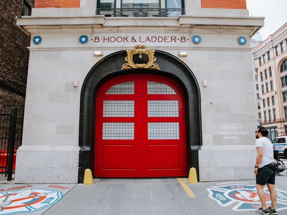 A man stands in front of the iconic red Ghostbusters Firehouse, showcasing its distinctive architecture and vibrant colour