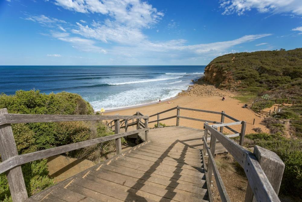 Wooden stairs lead down to a quiet Australian beach, with the ocean gently lapping at the shore in the background