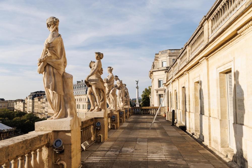 A row of statues on a balcony overlooking the Bordeaux cityscape