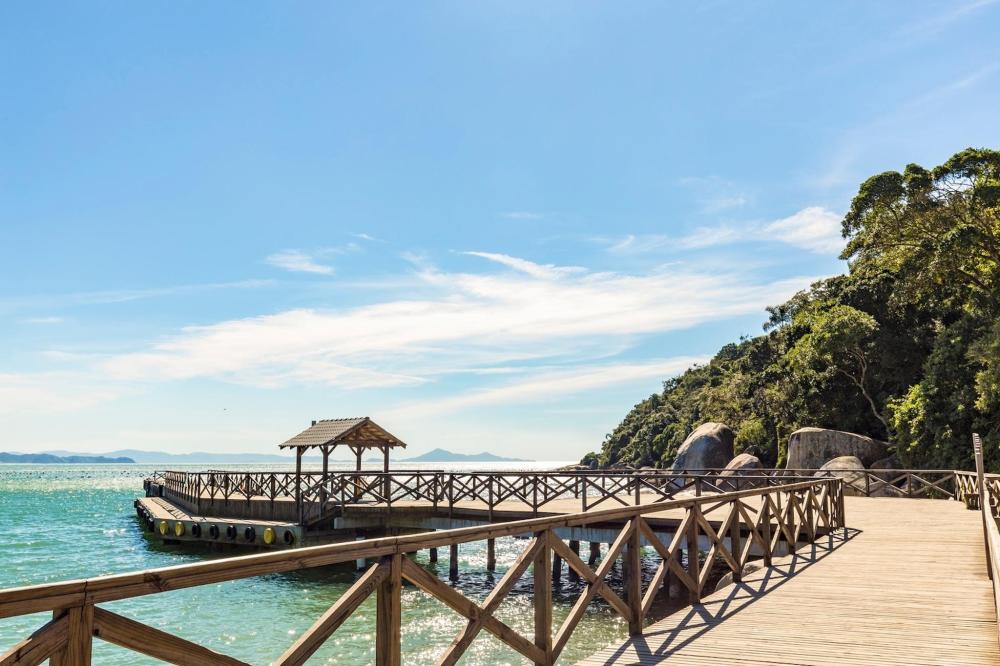 A wooden bridge leads to a gazebo over the ocean in Brazil, surrounded by calm waters and a clear blue sky