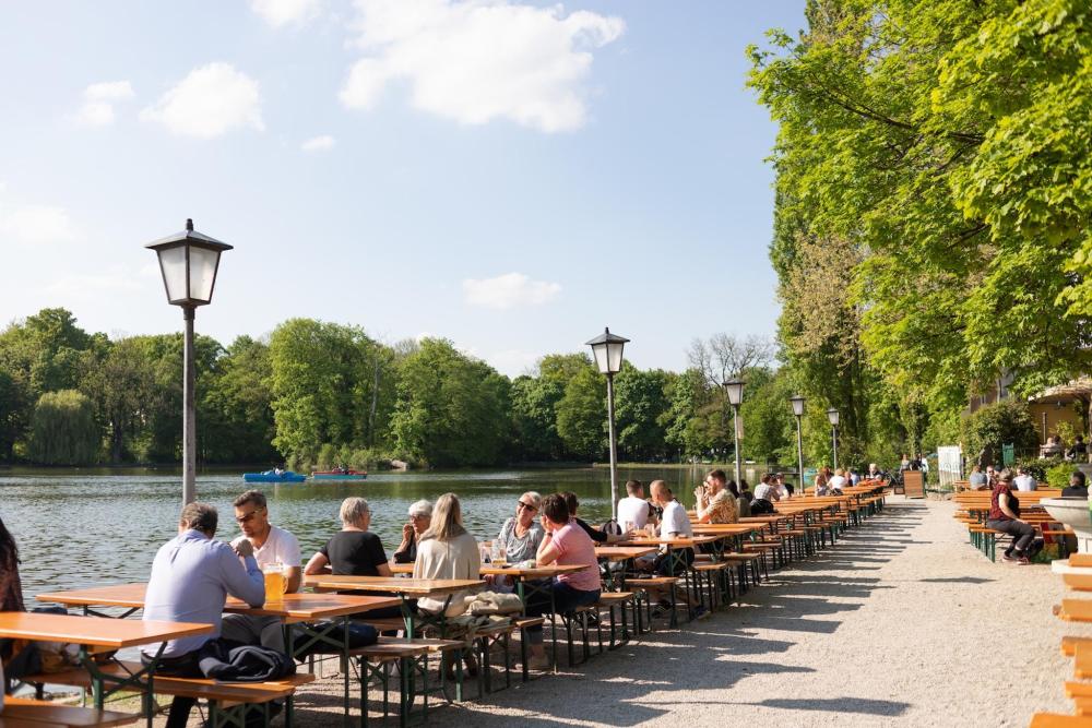 Several tables are lined up in a row, filled with people eating and drinking in the German sun