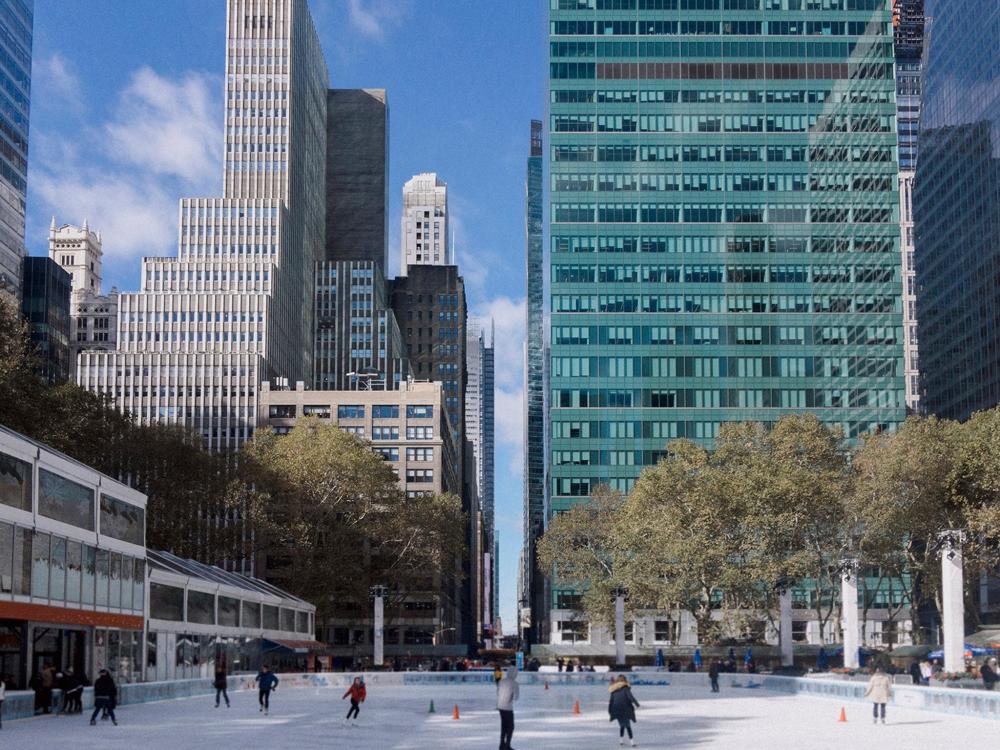 A bustling ice rink with tall buildings in the background, featuring people ice skating in Bryant Park