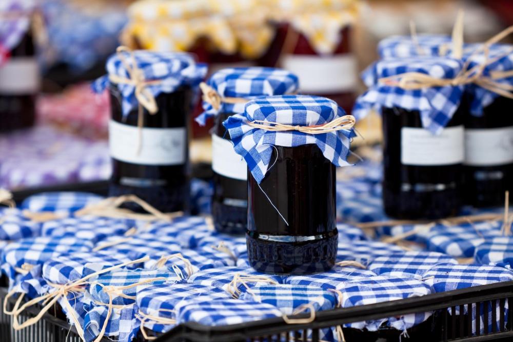 A variety of jam jars neatly arranged on display in a store with blue gingham lids