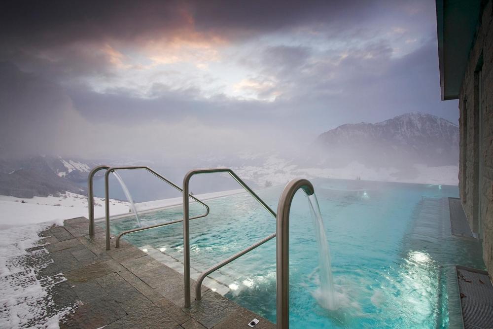A serene pool with water flowing into it, framed by majestic mountains at Hotel Villa Honegg, Switzerland.