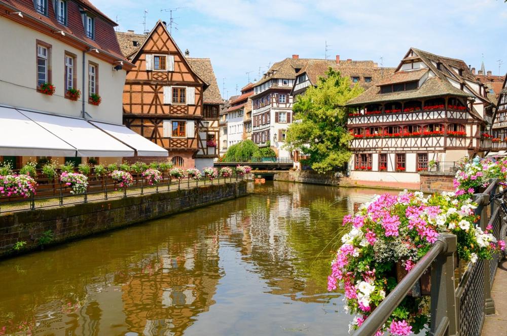 A picturesque river adorned with vibrant flowers, set against the festive backdrop of Strasbourg's Bastille Day decorations.