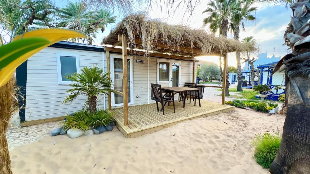 A small house with a patio and palm trees, part of the Cámping & Bungalows Estanyet resort.