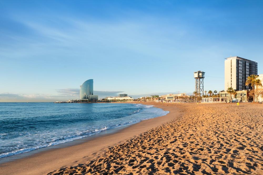A vibrant city beach in Barcelona is depicted. The sand has an orange hue and the sea is aquamarine.