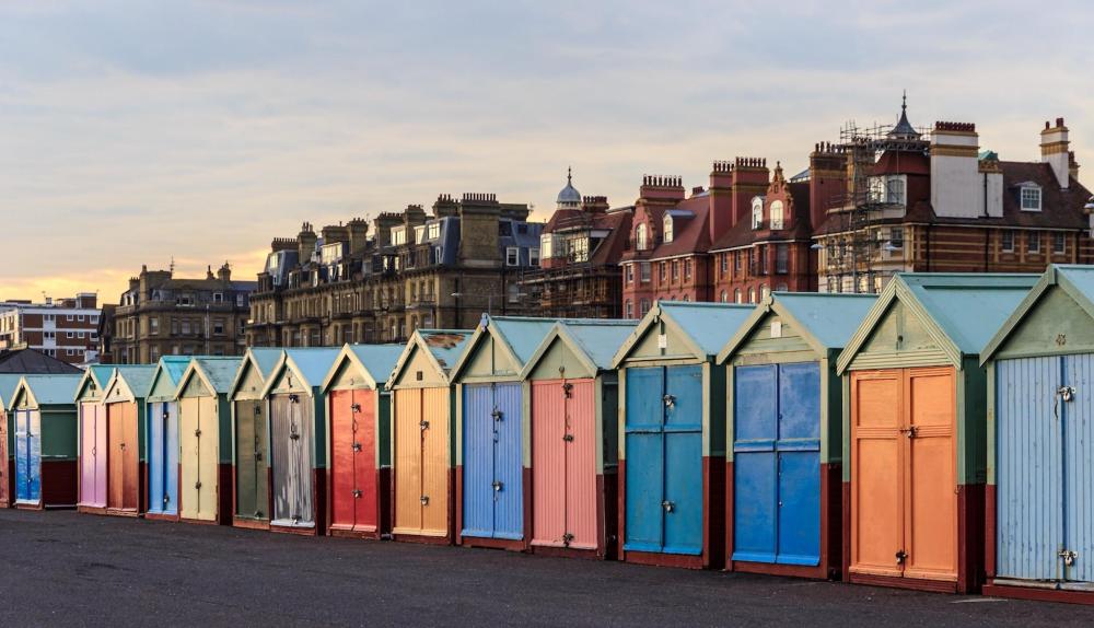 A row of vibrant beach huts in Brighton, showcasing a variety of colours against a clear blue sky