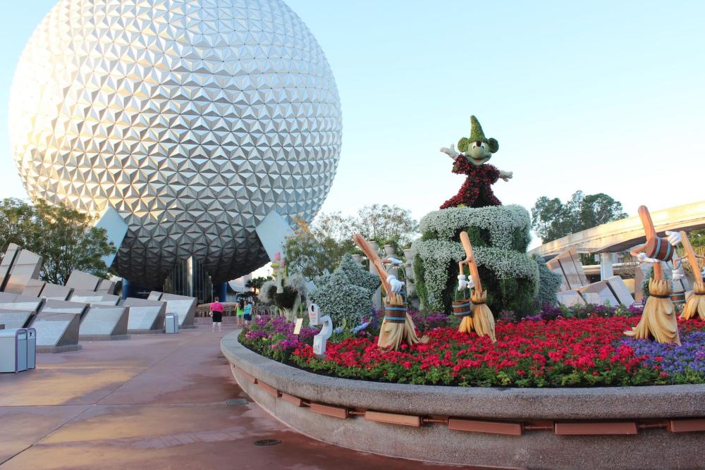 A flower bed with vibrant blooms and a flower statue of Mickey Mouse in front of the iconic dome at EPCOT, Disney World.