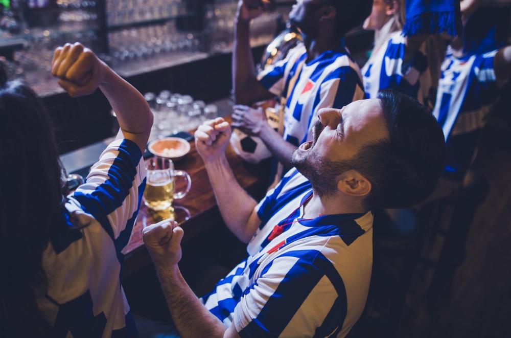 A group of football fans in blue and white shirts enthusiastically cheering at a sports bar in NYC