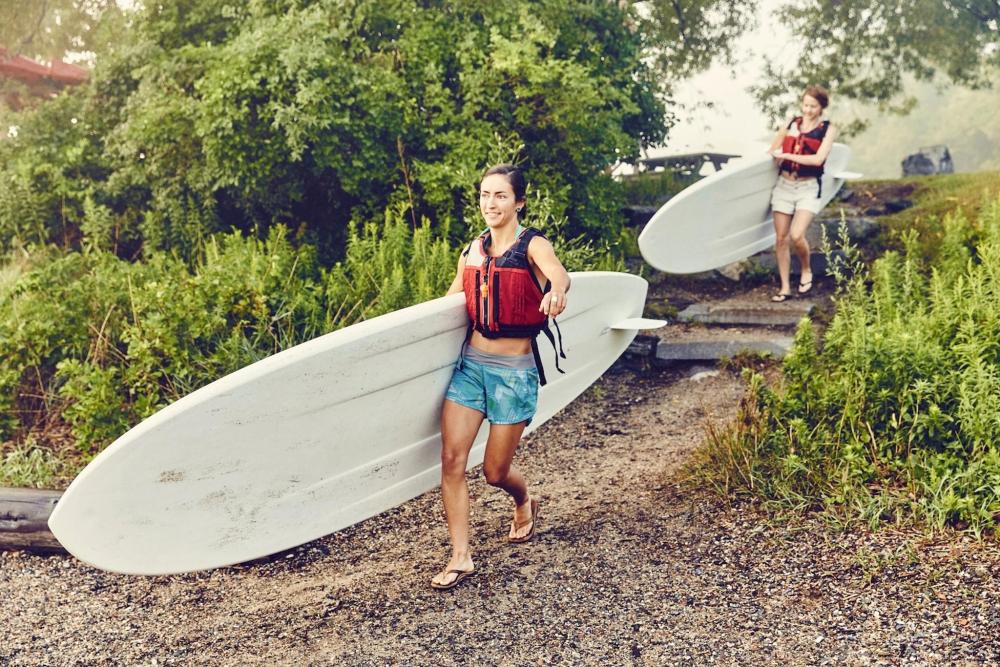 Two young women carry their paddle boards down to the water on a foggy day