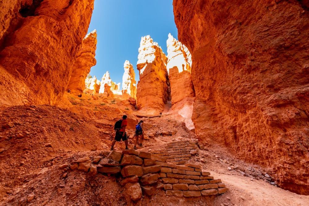 Two people walk along a path in Bryce Canyon National Park, surrounded by stunning rock formations and canyon views