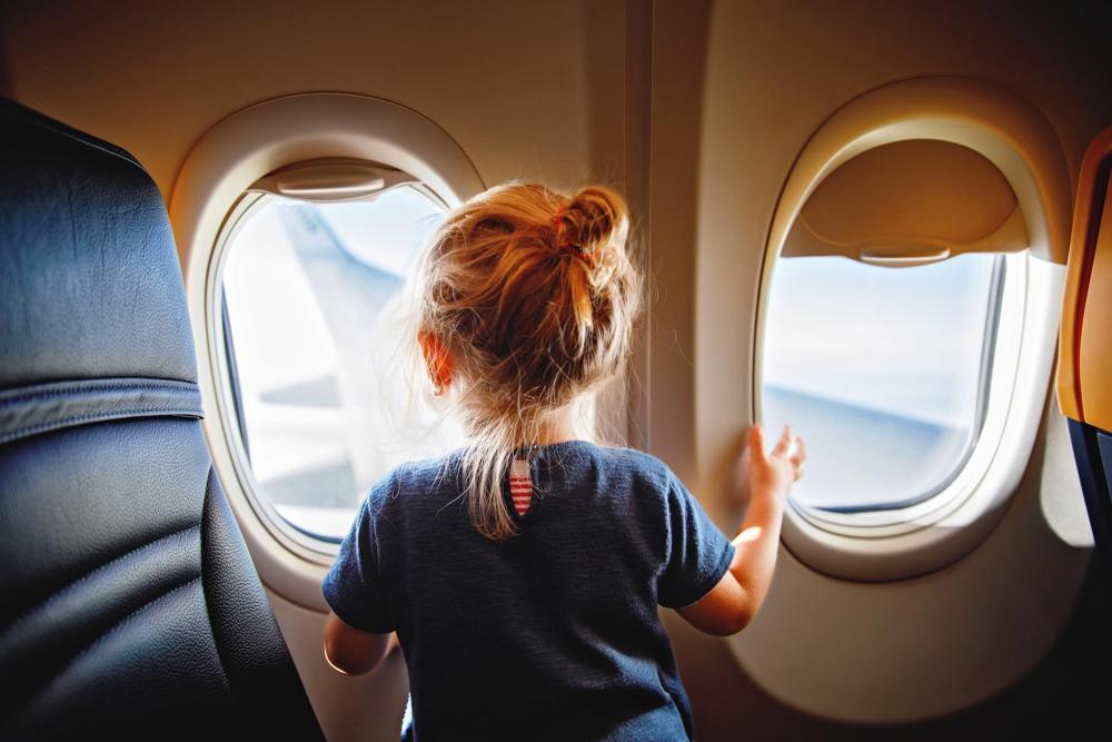 A little girl gazes out an airplane window, excitedly flying to Thanksgiving celebrations.