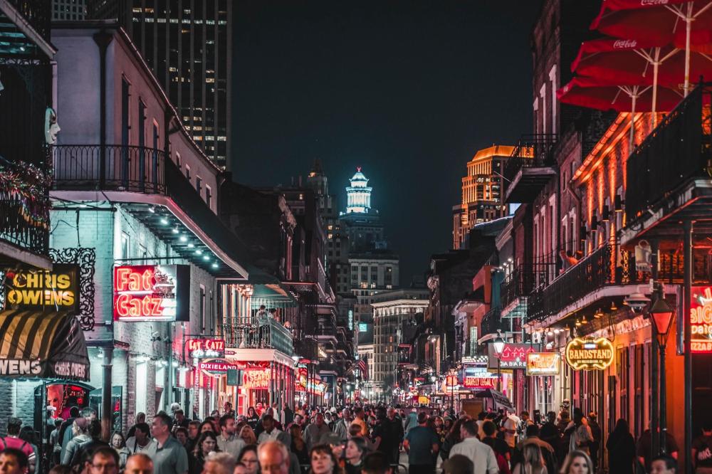 A bustling New Orleans street at night, filled with people walking and standing under vibrant city lights