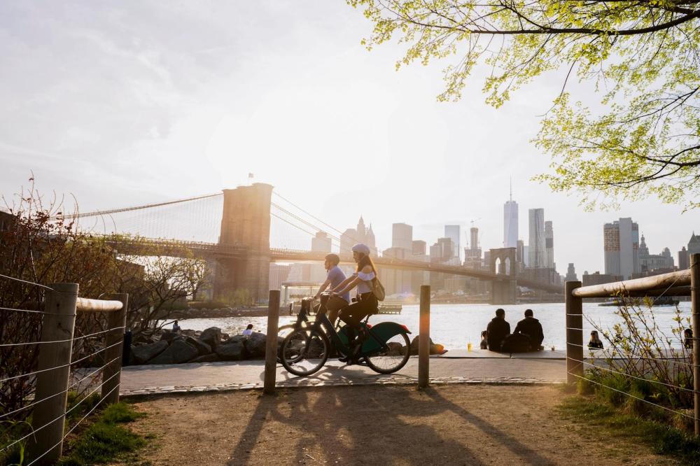 Two people cycling together near a bridge in NYC