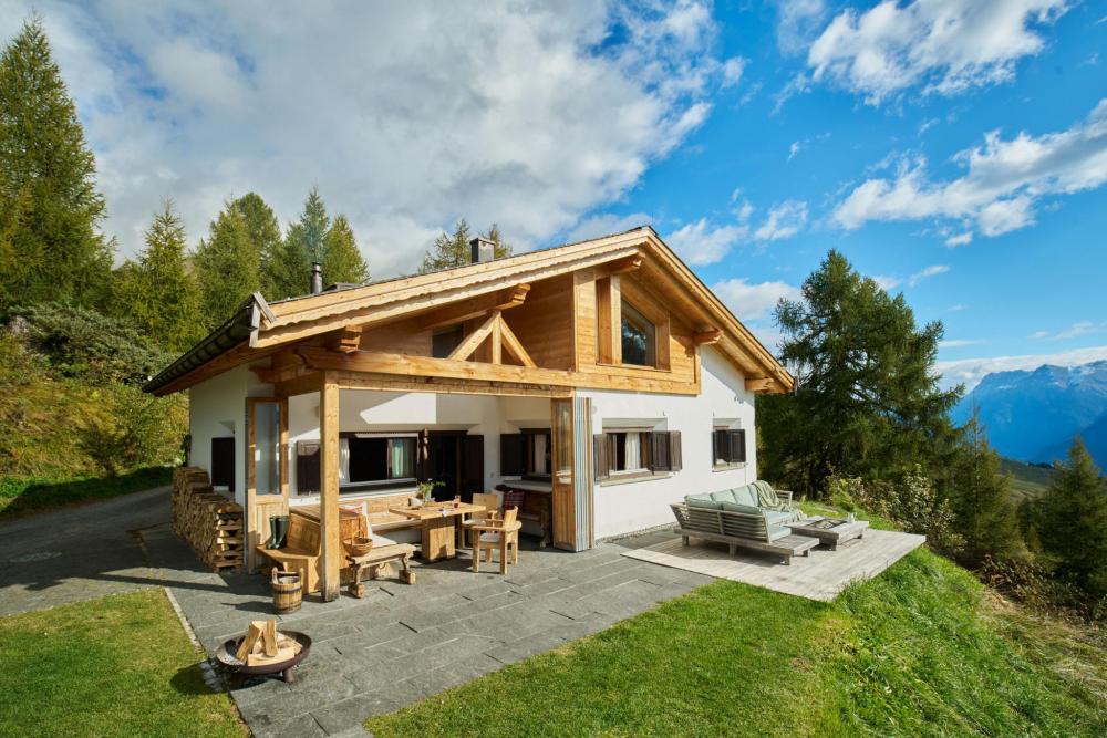 A wooden chalet with a patio, overlooking a scenic mountain view.