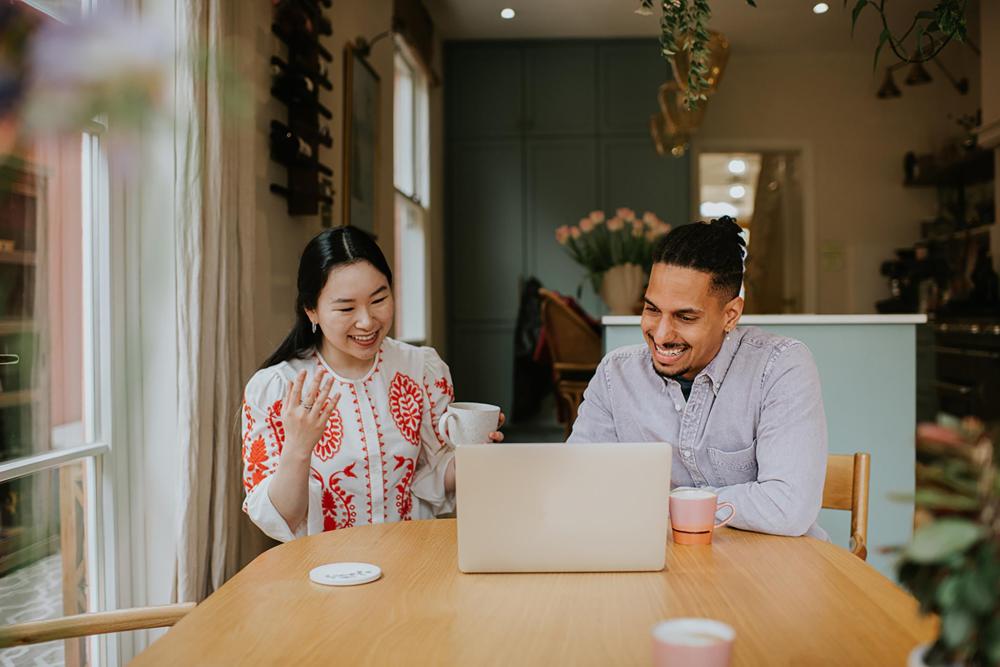 Couple sitting at a kitchen table, using a laptop to research tips for recognizing holiday home scams