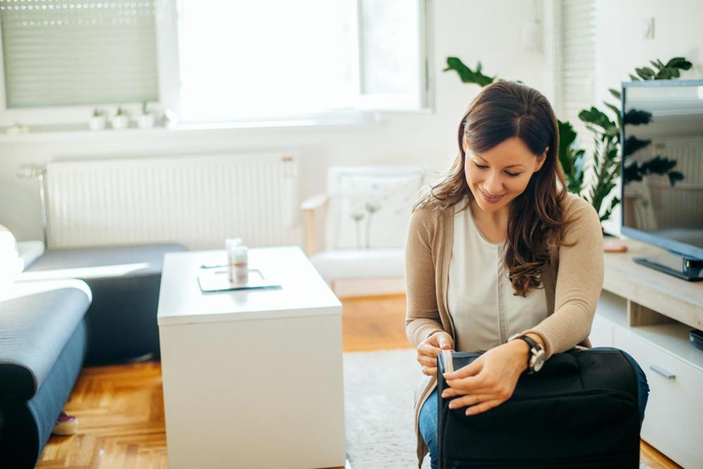 A woman measures her airplane luggage in her home. She smiles whilst measuring the depth of the case.
