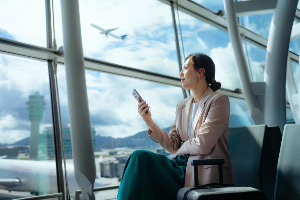Traveller sitting in an airport terminal using a smartphone while watching a plane take off