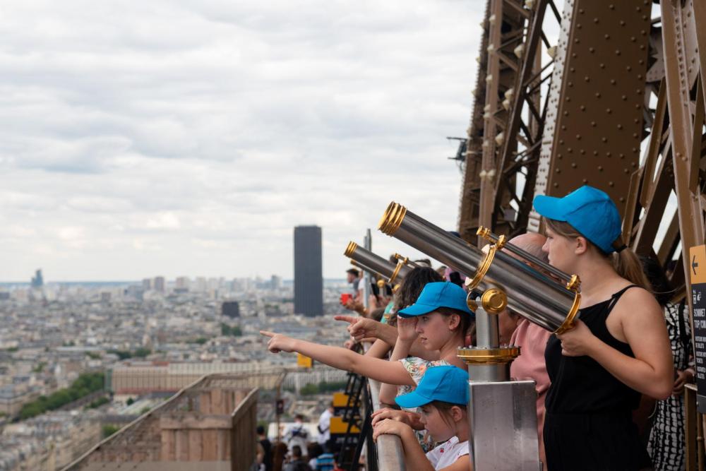 Children in blue baseball caps look through the telescopes from the observation deck of the Eiffel Tower in Paris, France.