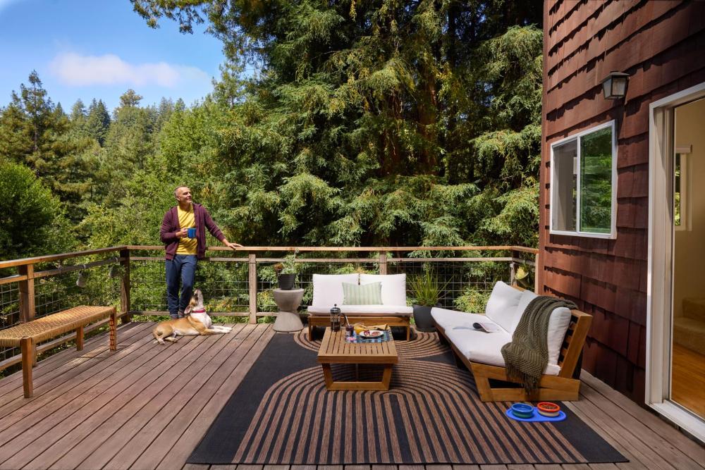 A man stands on a deck with a dog by his side.