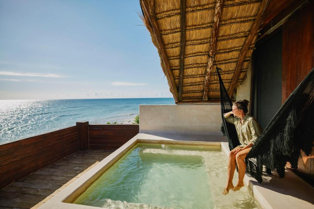 A woman relaxes in a hammock by a pool, with a stunning ocean view in the background.