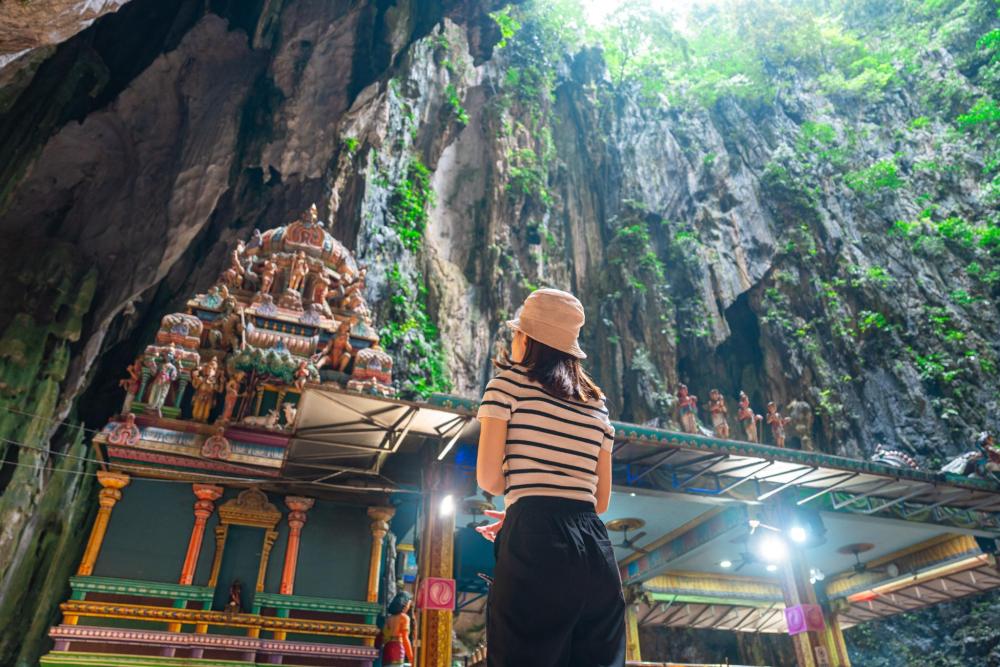 Visitor standing inside Batu Caves looking up at a colourful Hindu temple surrounded by towering limestone cliffs in Kuala Lumpur.
