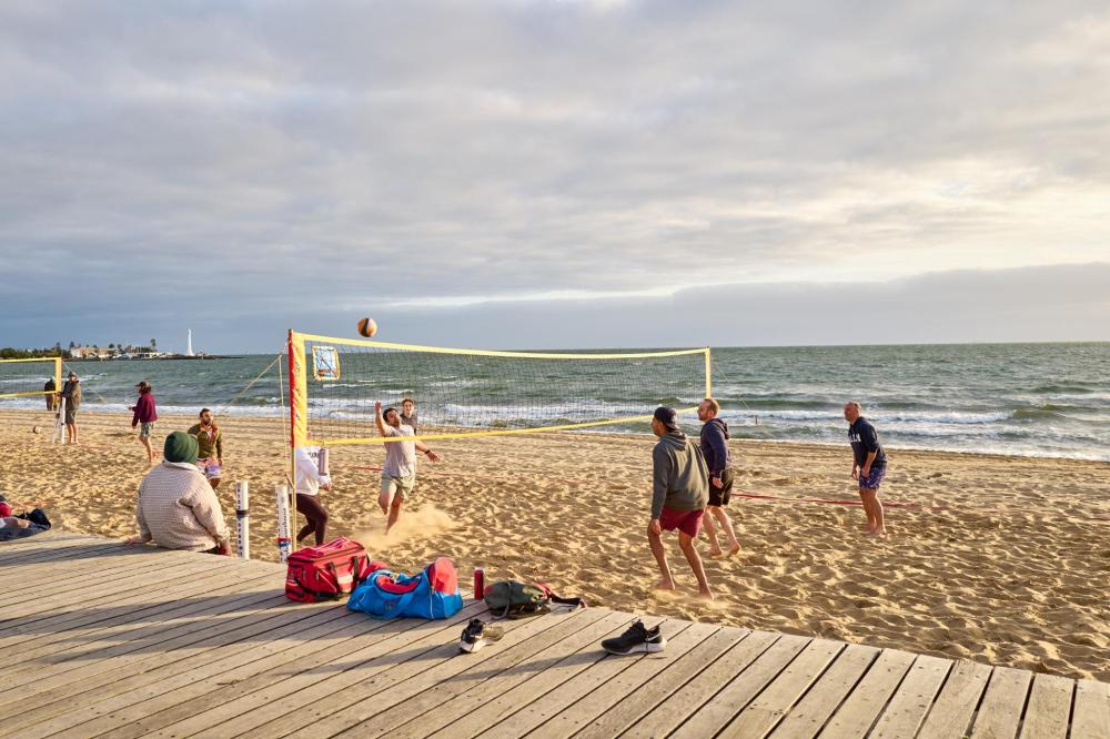 People playing beach volleyball on sandy beach by the ocean