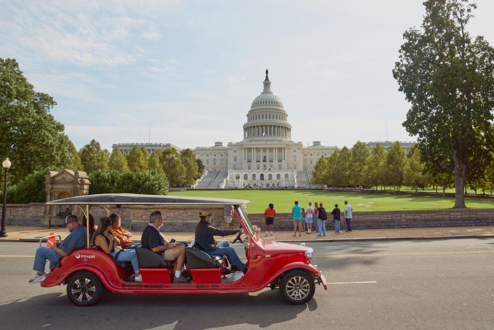 A red tour vehicle drives past the White House