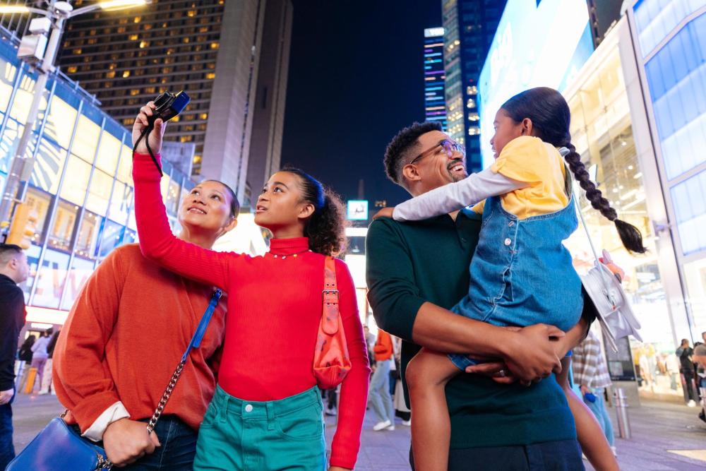 A family points at the sights in Times Square, surrounded by bright lights and bustling crowds