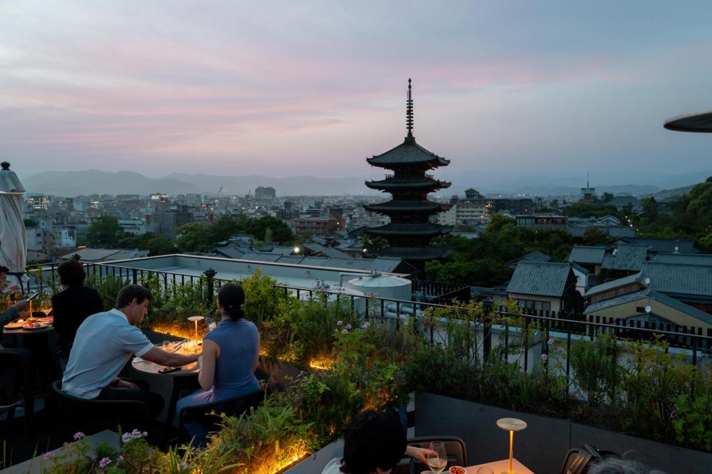 Couple dining on a rooftop terrace overlooking Kyoto skyline with a pagoda at sunset