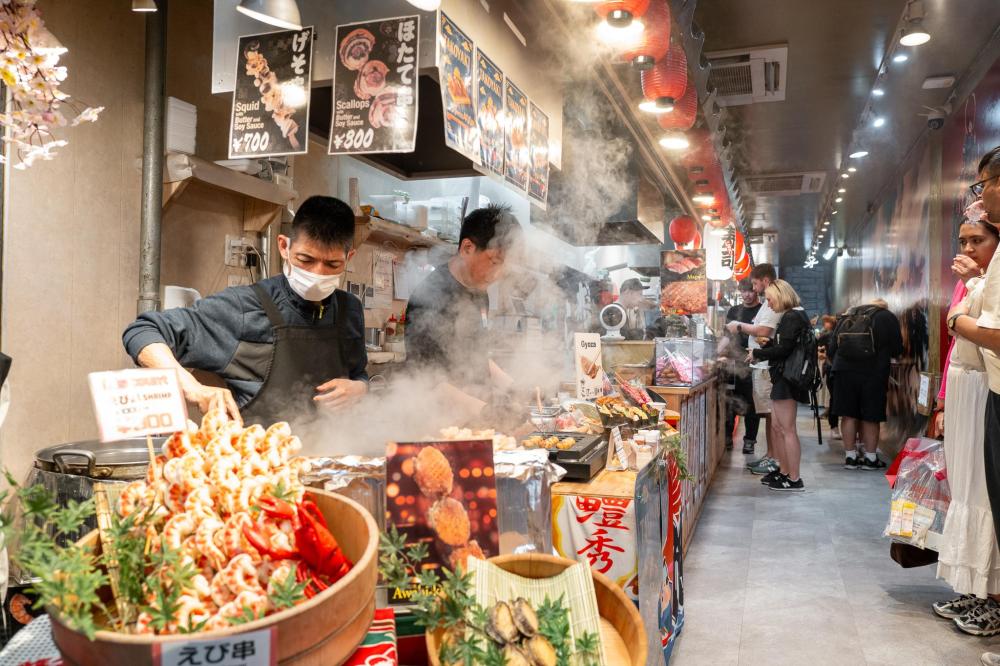 Busy Kyoto food market with chefs preparing street food and steam rising from grills