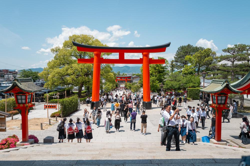 Crowds walking through a large red torii gate at a Kyoto shrine during a busy day