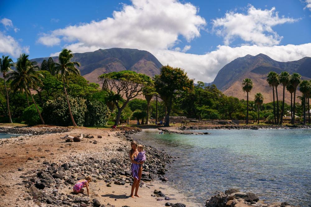Woman and children on a rocky Maui beach with mountains