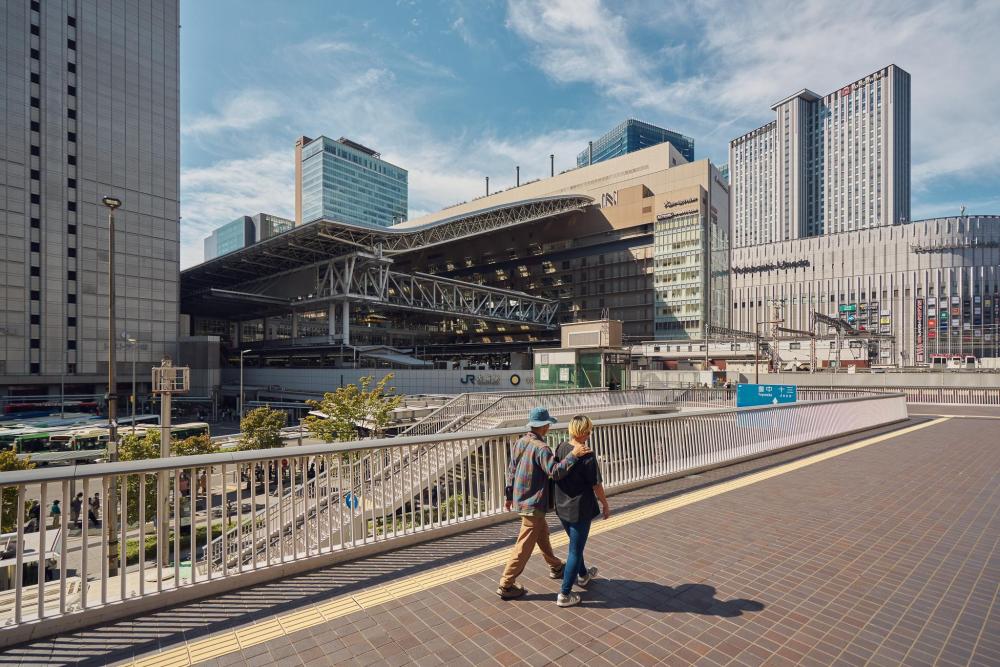 Two people walking past Osaka Station surrounded by modern buildings